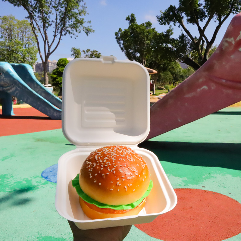 Open hinged food container holding a burger in an outdoor setting